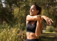 Mulher sorrindo com um top preto dentro de um parque se alongando, mostrando os benefícios da atividade física para a saúde mental