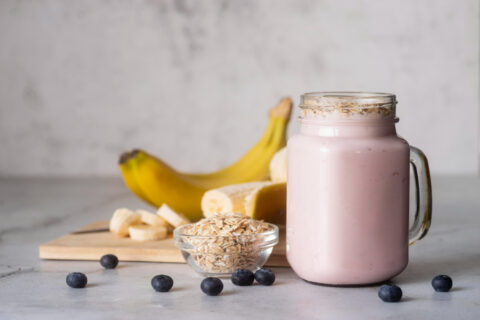 Smoothie rosa cremoso em copo de vidro, com creatina, banana, mirtilos e granola.