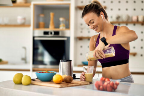 Mulher feliz e que pratica exercícios físicos prepara um smoothie de frutas e whey protein para o café da manhã.