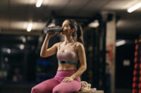 Mulher tomando shake de creatina após o treino em uma academia, representando a suplementação para recuperação muscular.