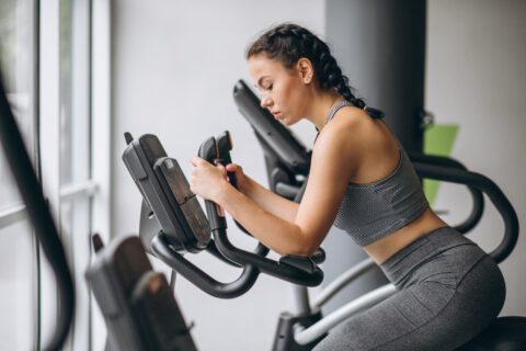 Mulher de cabelos presos faz exercício aeróbico em aparelho na academia para demonstrar se cardio é melhor antes ou depois do treino.