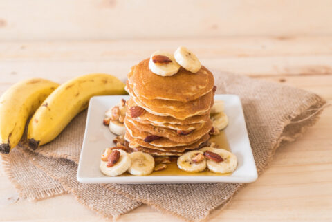 Bananas e panqueca de banana com whey protein em um prato branco quadrado sobre uma mesa.