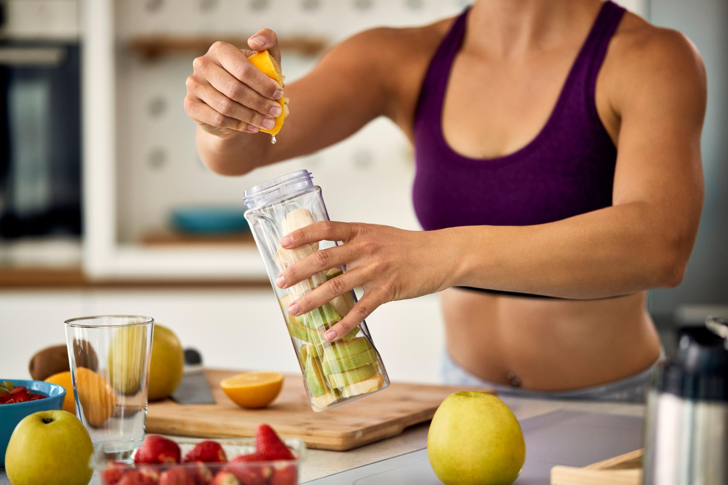 : Mulher com roupa de ginástica prepara um suco cheio de vitaminas usando maçã, limão e morangos.