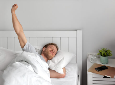 Um homem feliz acordando de manhã na cama após uma boa noite de sono e recuperação muscular