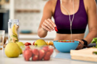 Mulher com roupa de treino preparando sua alimentação com muitas frutas na cozinha