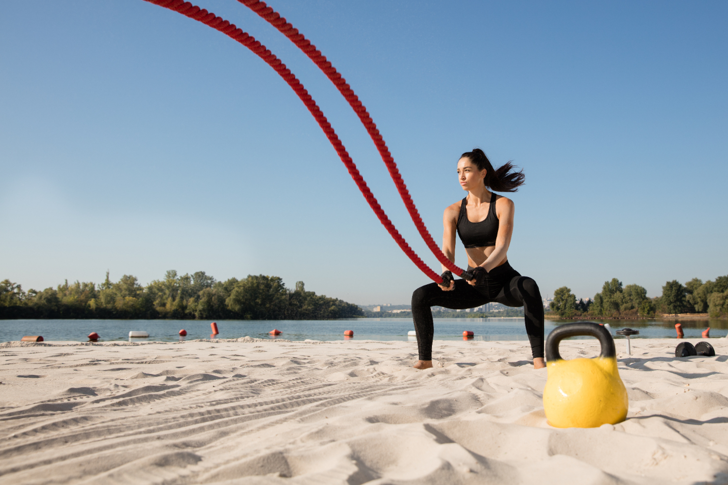 Mulher praticando exercícios físicos na praia em um dia de sol e usando cordas de batalha mostra a importância e os benefícios da vitamina C no verão para proteger a pele.