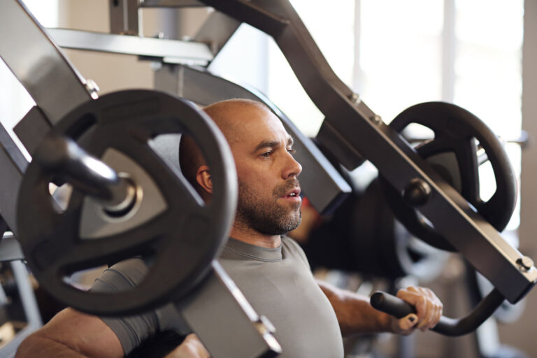 Homem com uma camiseta cinza puxando peso em uma academia com o método cluster set