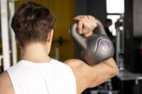 Homem de regata branca treinando com kettlebell, mostrando a importância de exercícios para prevenir o catabolismo muscular