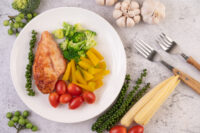 Prato saudável com frango grelhado, brócolis, tomate-cereja e legumes, ideal para manter o déficit calórico e uma alimentação equilibrada.