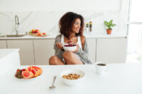 Mulher afrodescendente toma café da manhã saudável, com frutas vermelhas e granola, para se preparar para a rotina de exercícios do dia
