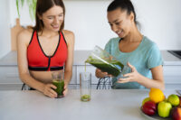 Duas mulheres com roupas esportivas preparando receitas de sucos detox.