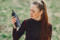 Mulher com roupa esportiva segura uma garrafa como se perguntasse se pode tomar whey sem treinar