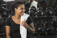 Mulher com roupa de ginástica e toalha no pescoço voltando aos treinos em uma academia.