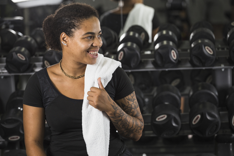 Mulher com roupa de ginástica e toalha no pescoço voltando aos treinos em uma academia.